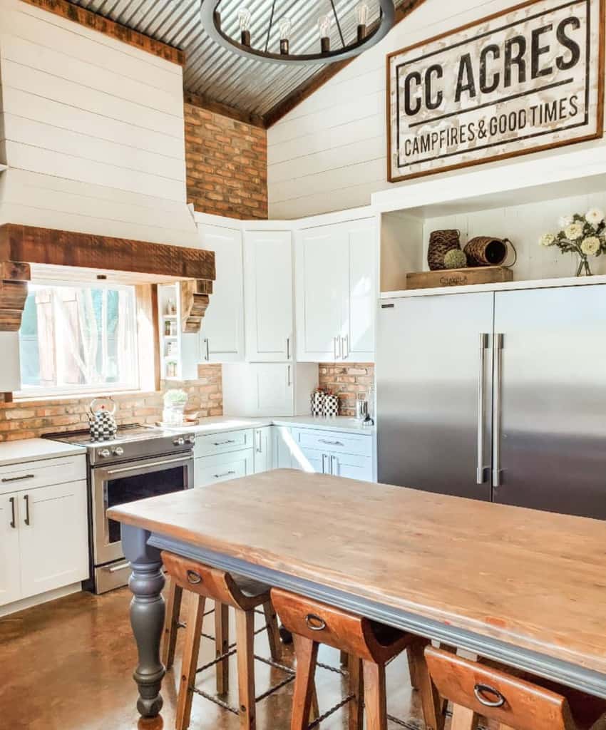 Rustic farmhouse kitchen with a 'CC Acres Campfires & Good Times' wood sign, brick accents, white cabinets, and a wooden island