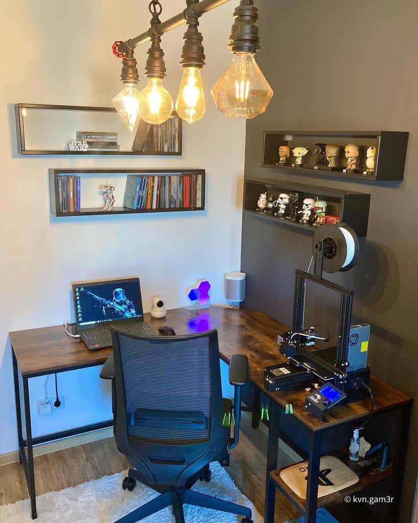 Modern home office with a wooden desk, laptop, 3D printer, shelves with collectibles, books, and hanging Edison bulbs for lighting