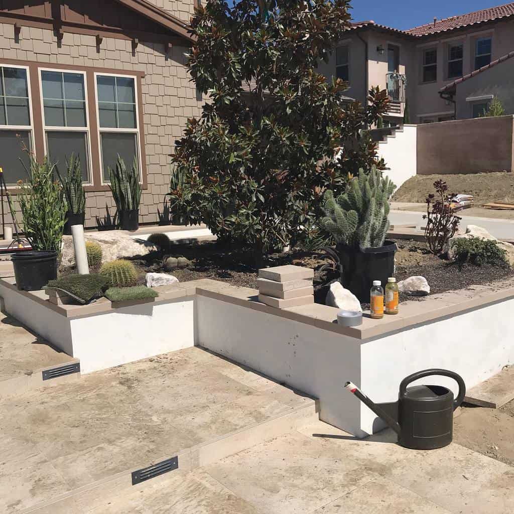 Modern front yard xeriscape with raised planters, drought-tolerant plants, succulents, and a watering can on a stone patio