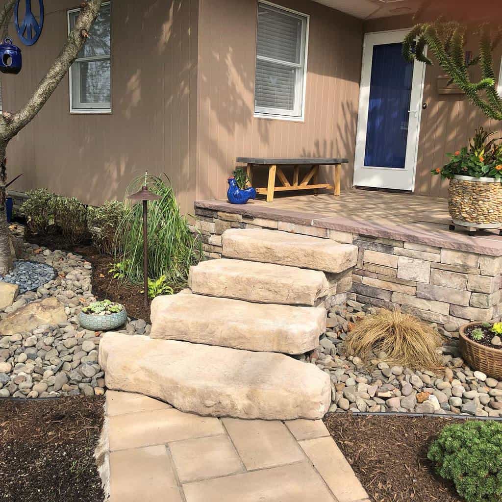 Charming xeriscape front porch with stone steps, drought-tolerant plants, river rocks, and a blue door adding a pop of color