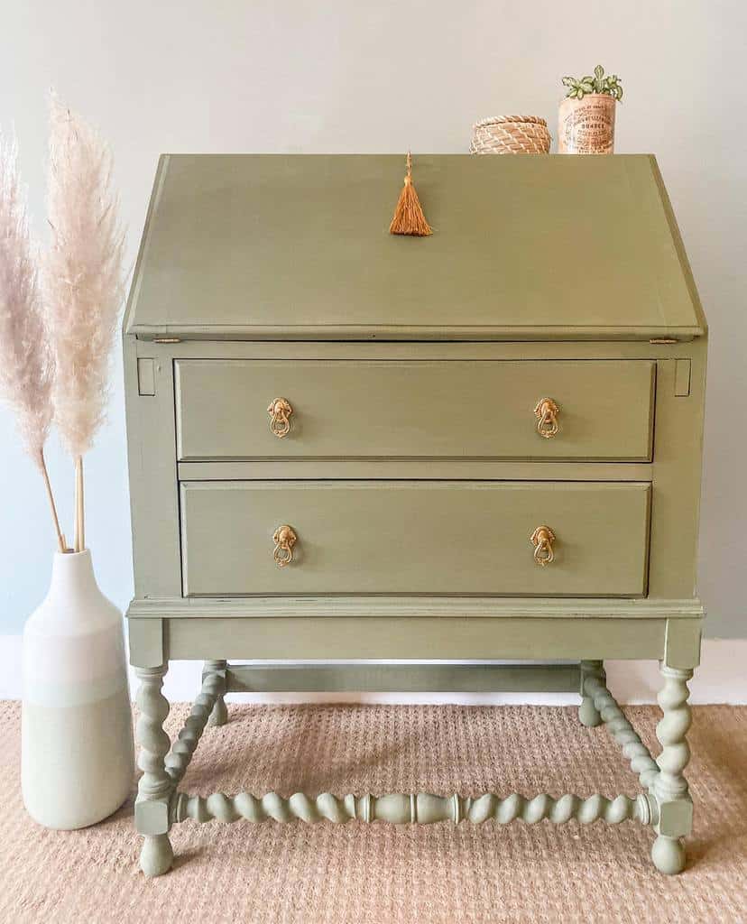 Vintage sage green chalk-painted secretary desk with gold hardware, spindle legs, and a tassel accent, styled with neutral decor