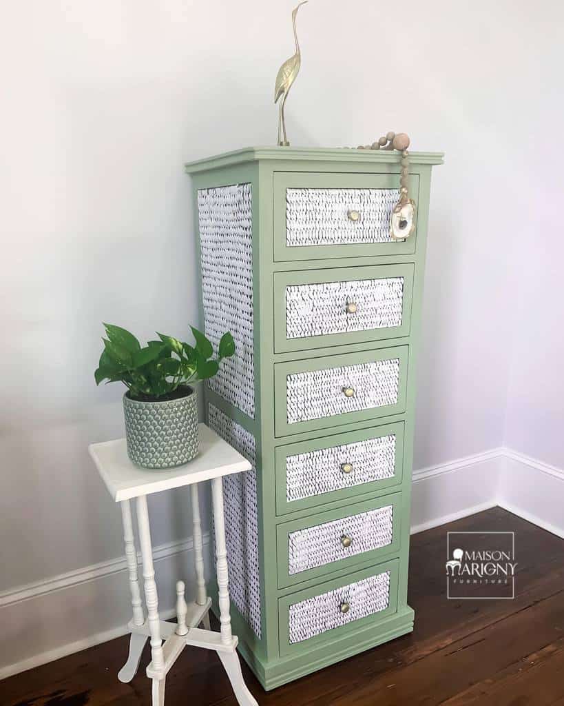 Sage green chalk-painted tall dresser with woven-texture drawer fronts, gold knobs, and coastal decor, styled with a white side table and plant