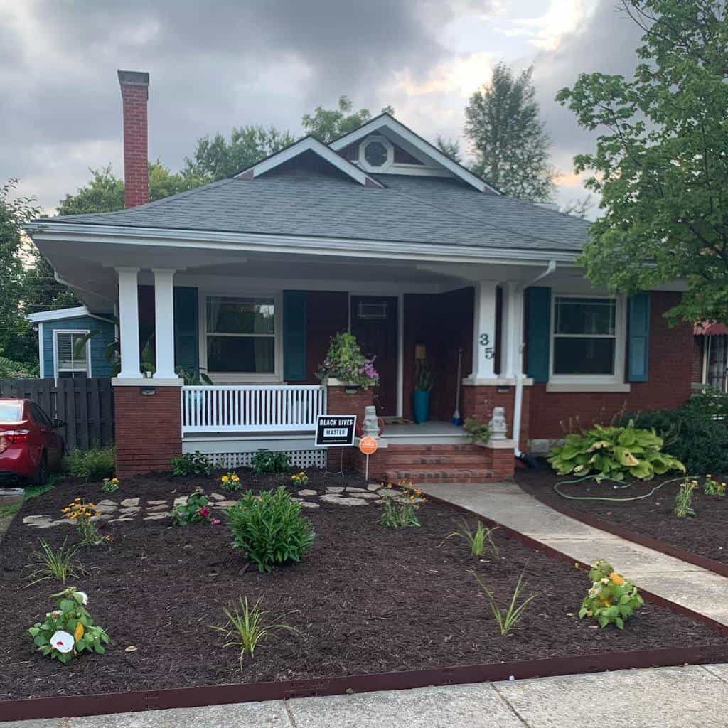 Charming front yard xeriscape with mulch, drought-tolerant plants, a brick walkway, and a cozy porch on a traditional home