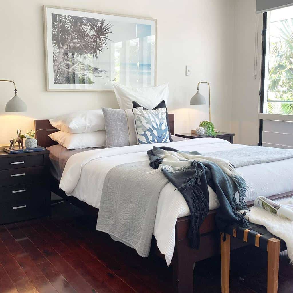 Cozy bedroom with a neatly made bed, pillows, and blankets, framed ocean photo on the wall, ambient lighting and decor accents