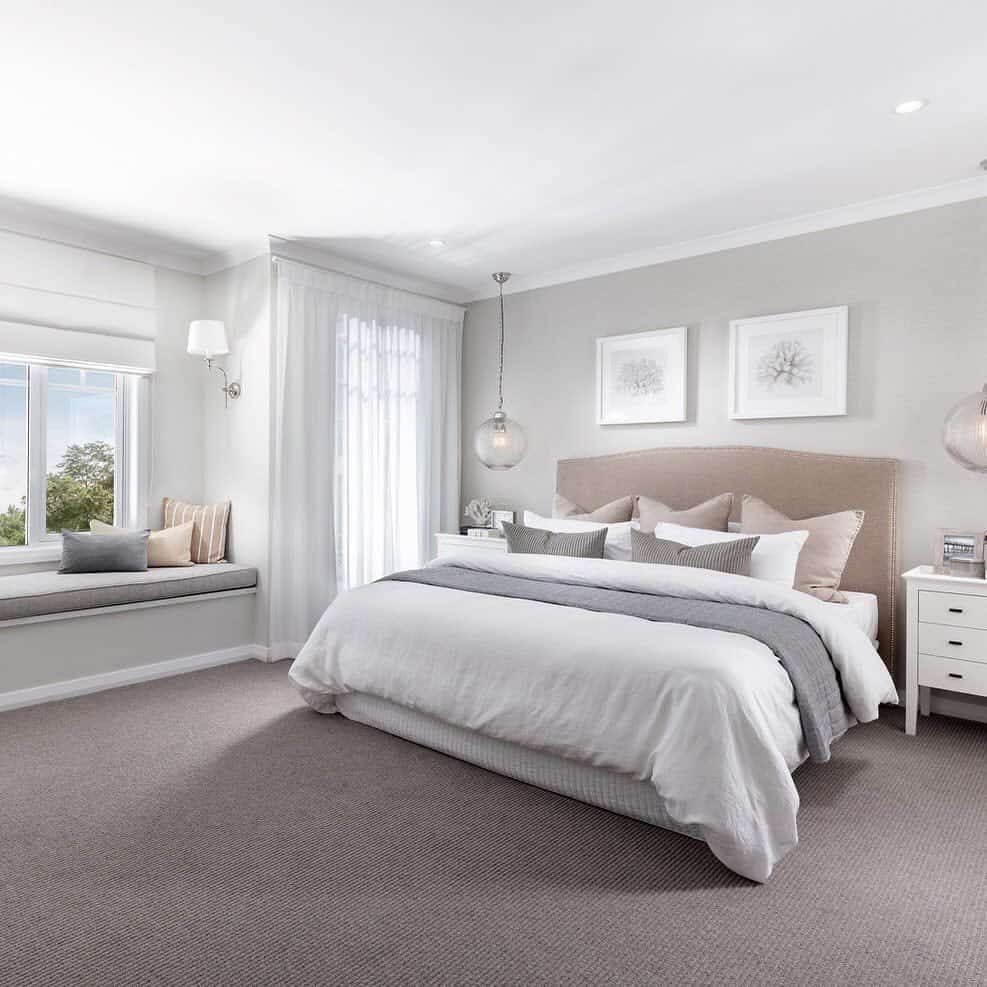 Bright, modern bedroom with a large bed, neutral tones, wall art, and a window seat with a view