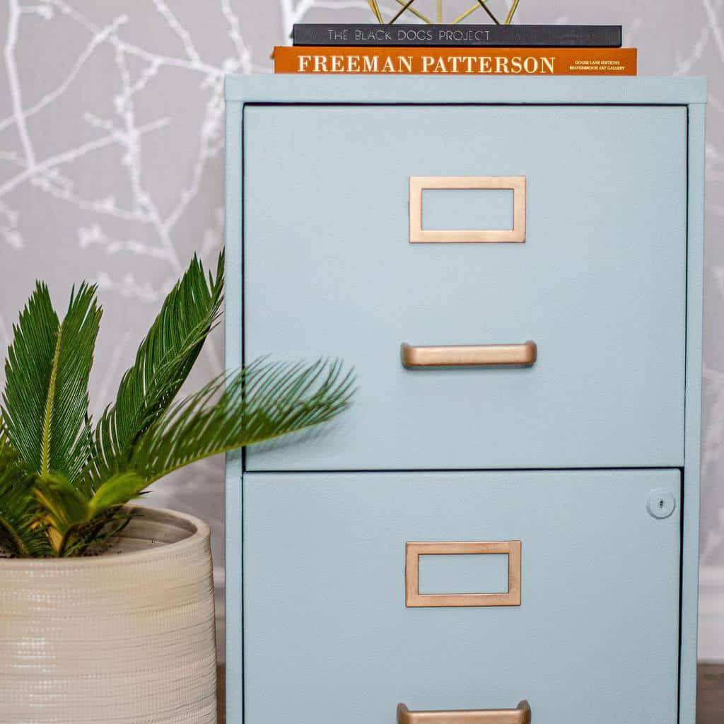 Light blue chalk-painted filing cabinet with gold hardware, styled with books and a modern decor piece, set against a patterned wall