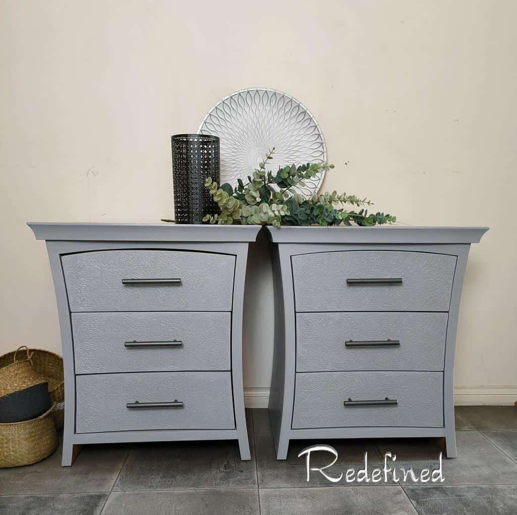 Pair of modern gray chalk-painted nightstands with curved frames, textured drawer fronts, and sleek black handles, styled with greenery and decor