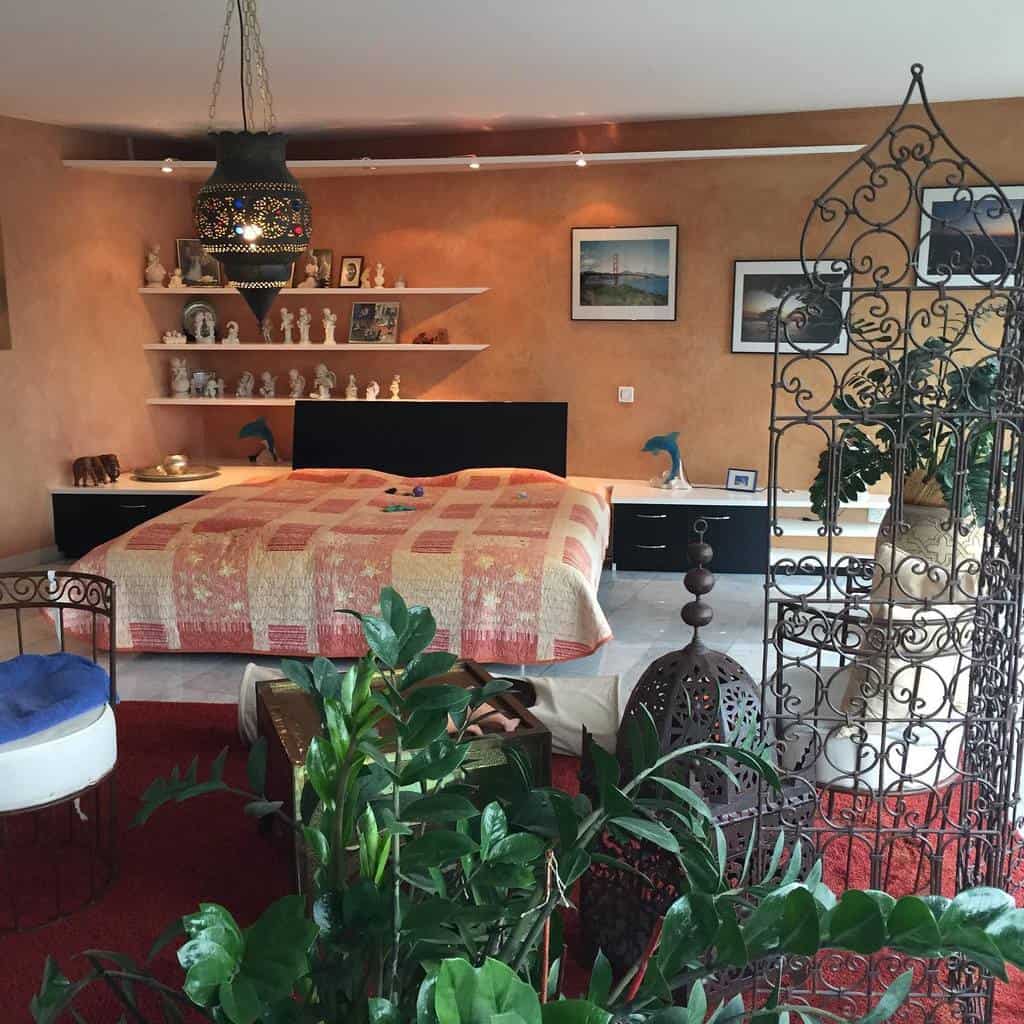 Eclectic bedroom with plants, a wrought iron room divider, Moroccan-style lamp, and artwork on the walls