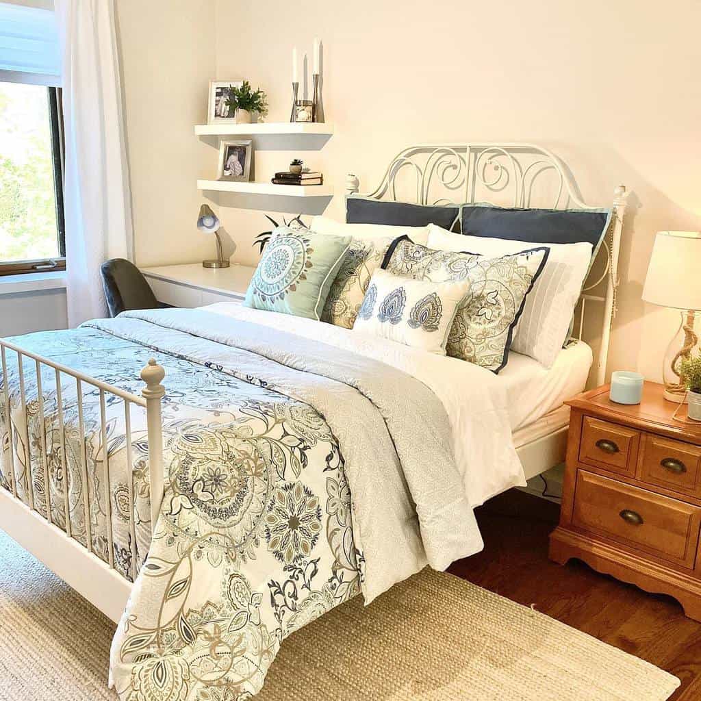 Cozy bedroom with patterned bedding, white iron bed frame, wooden nightstand with a lamp, and wall shelves with decor