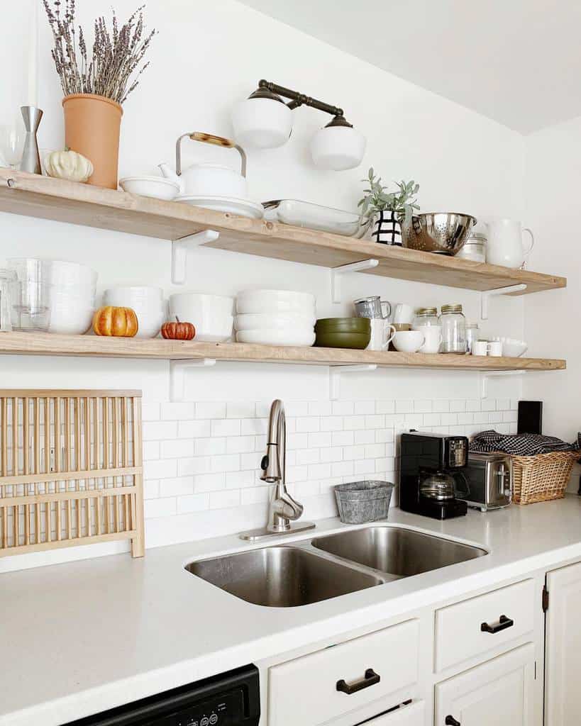 Minimalist kitchen with white subway tiles, wooden shelves holding dishes and decor items, a double sink, and a black coffee maker