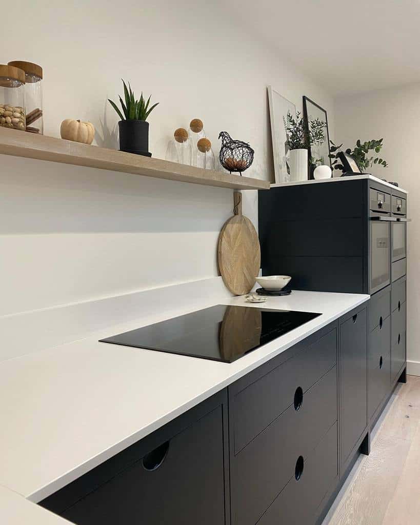 A sleek wooden floating shelf displays glass jars, plants, and minimalist decor, complementing the modern black and white kitchen design