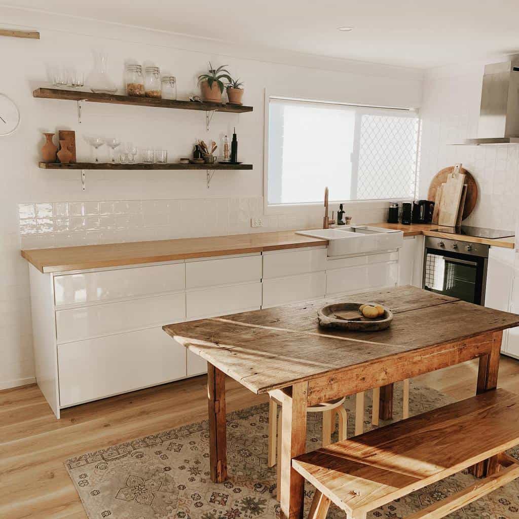 Rustic wooden shelves with metal brackets hold glassware, jars, and plants, adding charm to a minimalist white and wood farmhouse kitchen