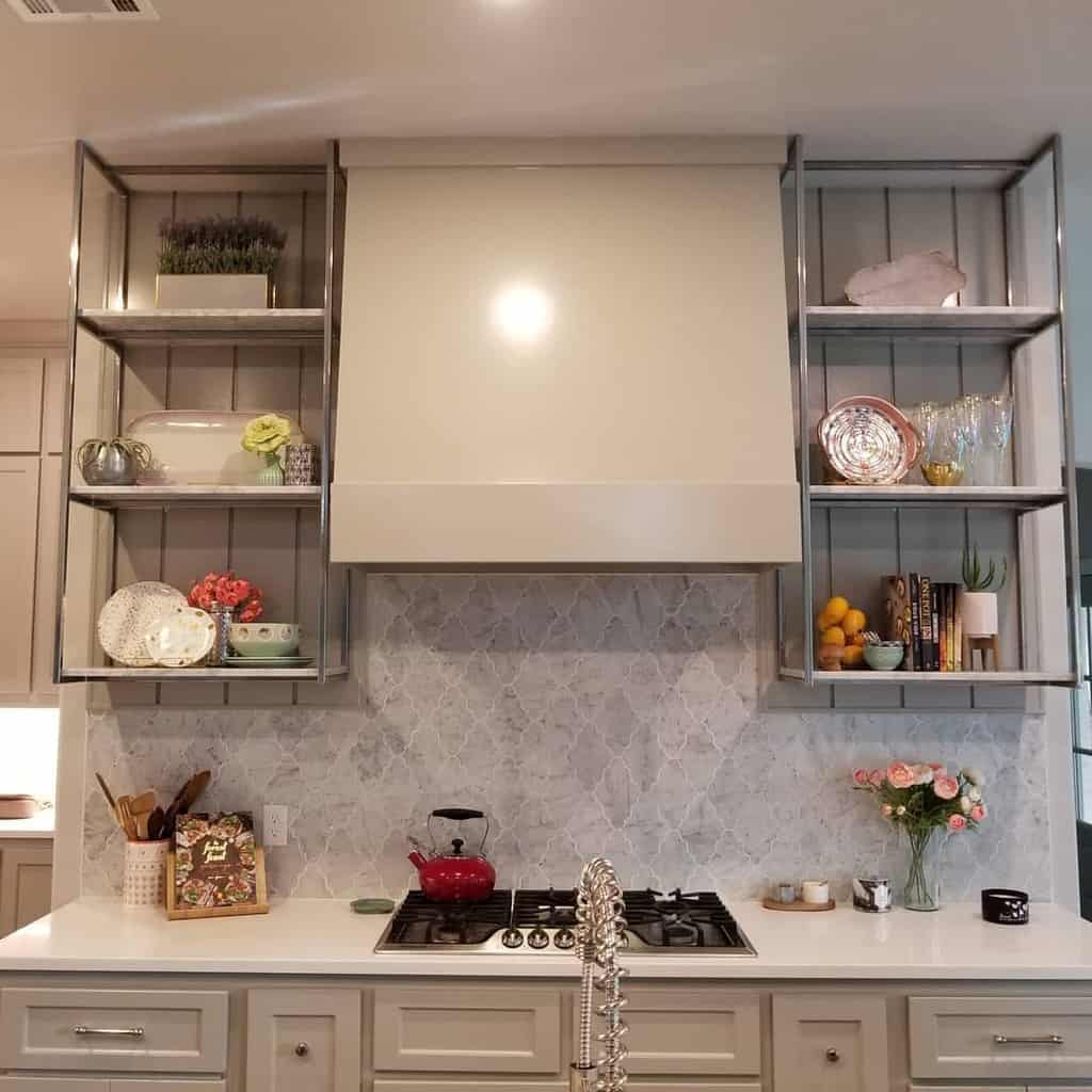 Metal-framed open shelves hold decorative plates, glassware, and small plants, adding elegance to a neutral-toned kitchen with a marble backsplash