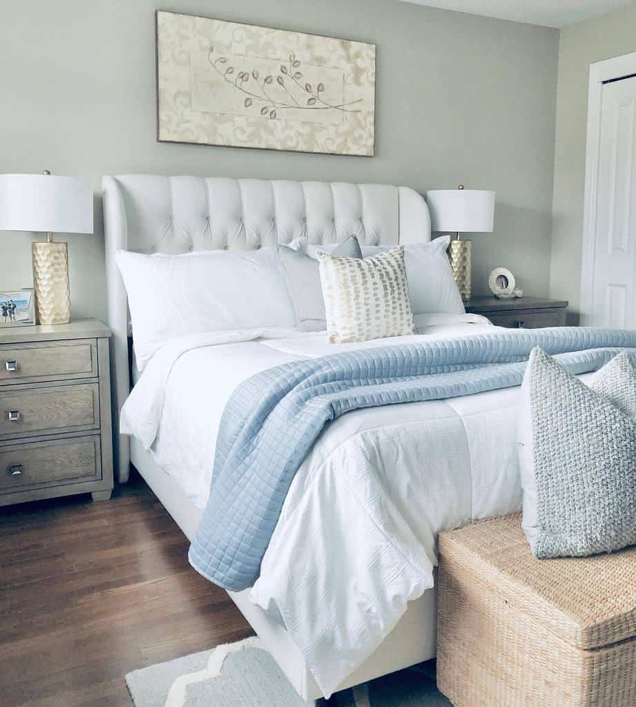 Cozy bedroom with a white and blue theme, featuring a cushioned bed, decorative pillows, nightstands, and a wall art piece above the bed