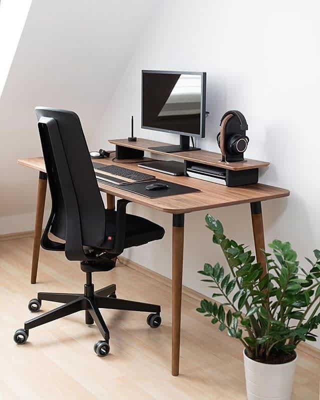 Minimalist home office with a wooden desk, chair, monitor, keyboard, and headphones; potted plant on the floor; bright, modern space