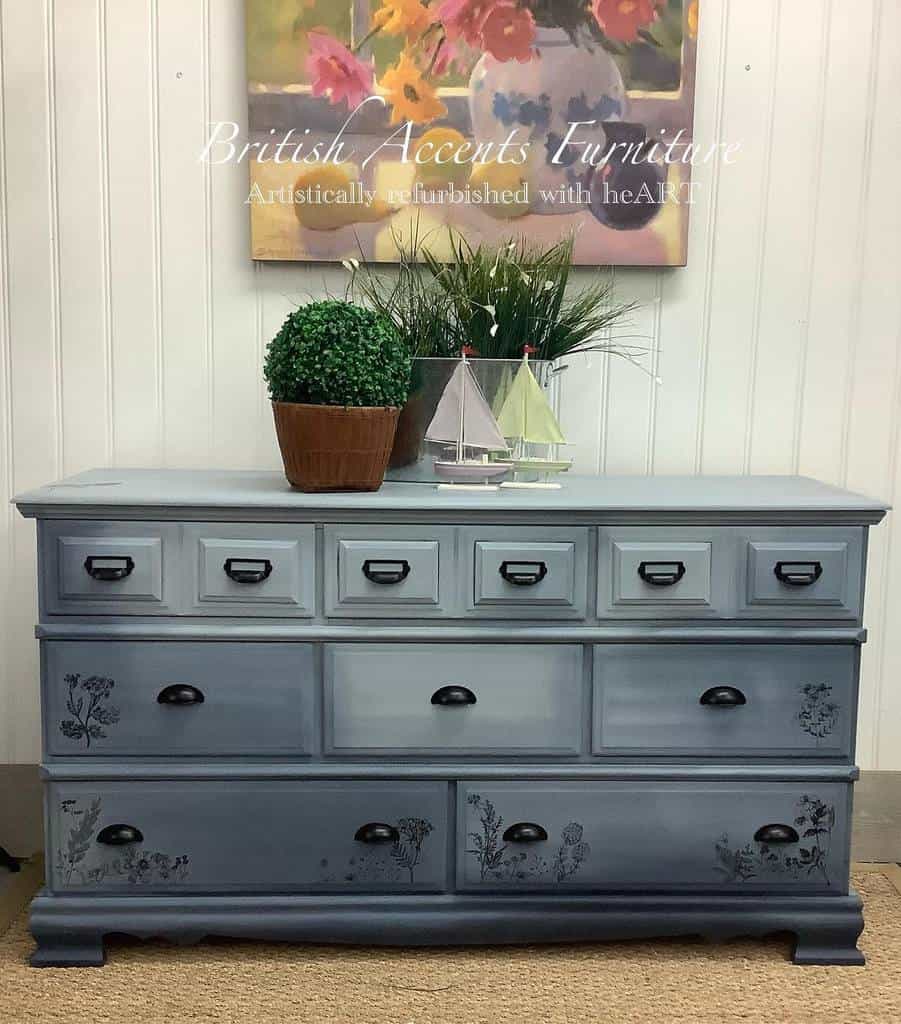 Ombre blue chalk-painted dresser with black hardware and delicate floral detailing, styled with greenery, sailboat decor, and a floral painting