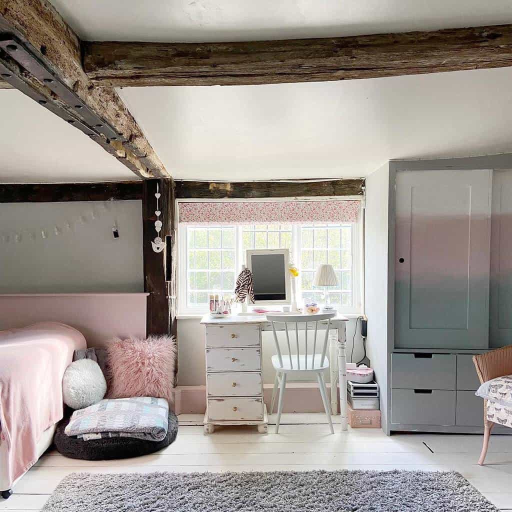 Cozy attic bedroom with rustic beams, featuring an ombre chalk-painted wardrobe, a white writing desk, and soft pastel decor