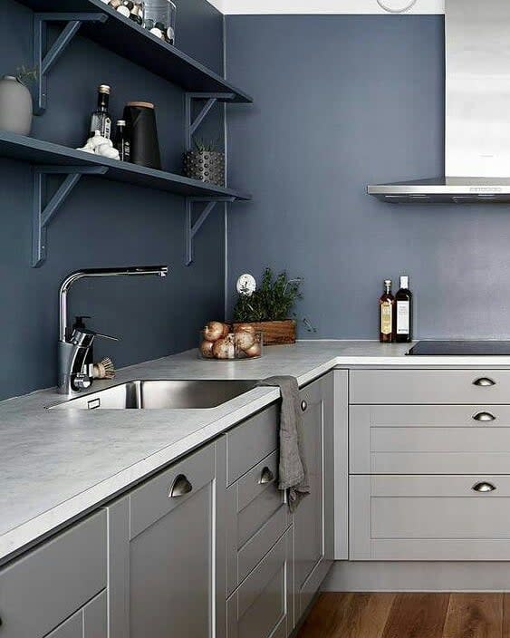 Modern kitchen with gray cabinets, white countertop, stainless steel sink, and open shelving with decor against a blue wall