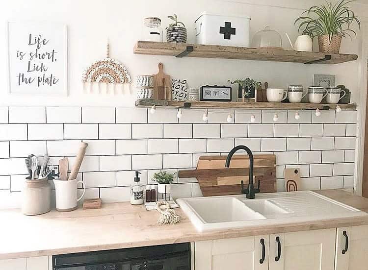 Rustic wooden shelves with black brackets hold plants, mugs, and decor, adding warmth and charm to a farmhouse-style kitchen with subway tiles