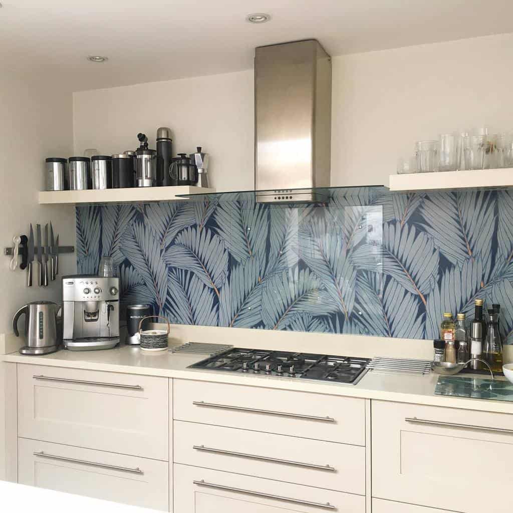 Minimalist white floating shelves hold glassware and coffee essentials, complementing a modern kitchen with a bold tropical leaf backsplash