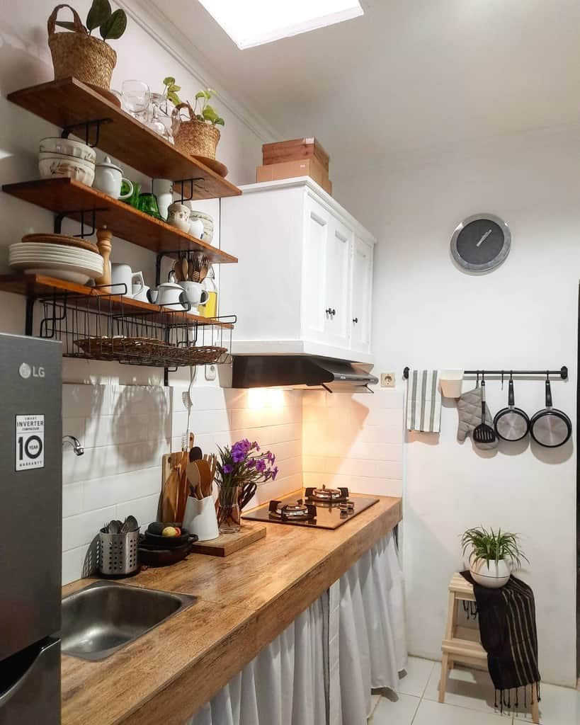 Rustic wooden shelves with black metal brackets hold dishes, glassware, and potted plants, adding charm to a compact farmhouse-style kitchen