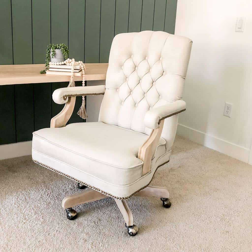 Elegant tufted office chair with cream chalk-painted fabric and natural wood accents, styled in a modern workspace with a green paneled wall