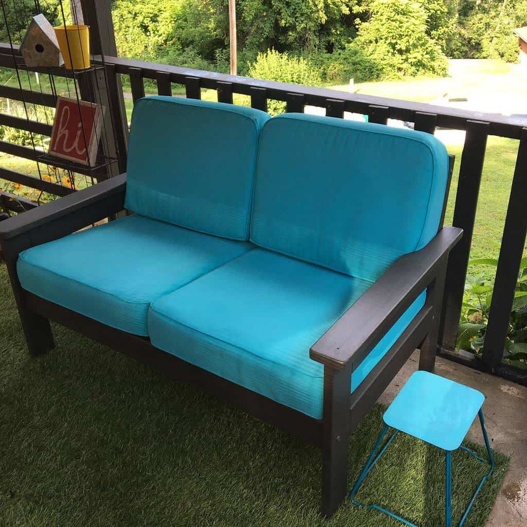 Outdoor loveseat with bright turquoise chalk-painted cushions and a dark wooden frame, styled with a matching blue metal stool on a porch