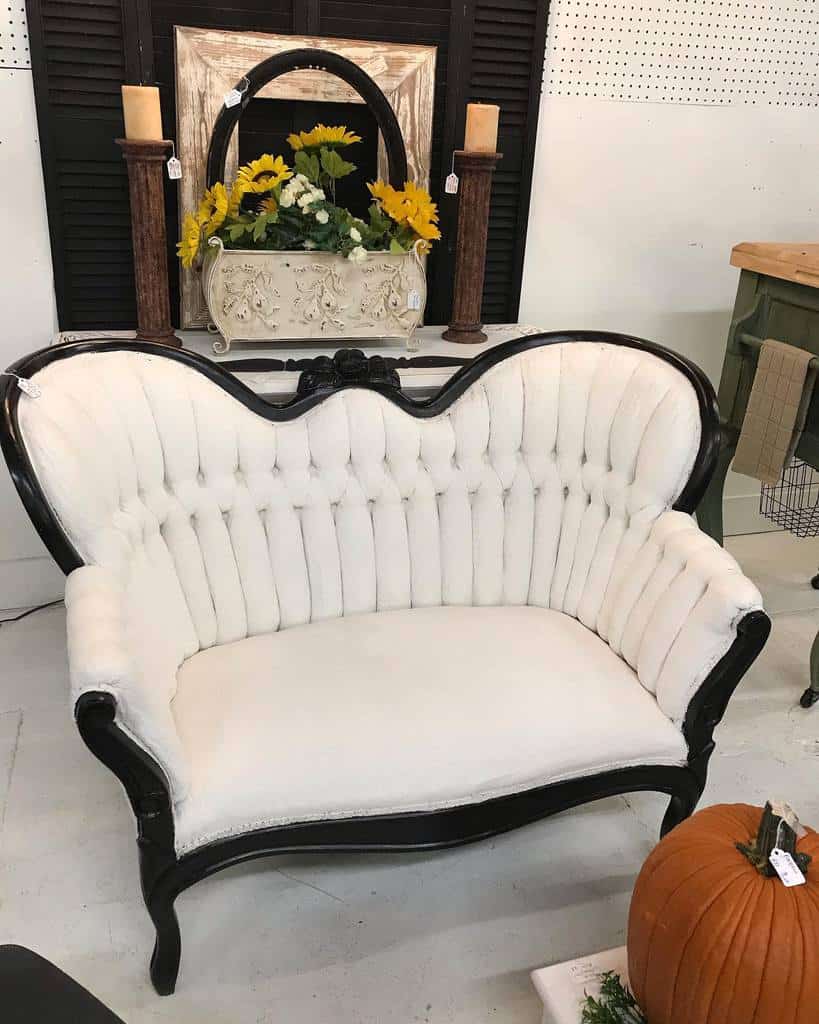 Vintage tufted loveseat with chalk-painted white fabric and a glossy black frame, styled with sunflowers, candles, and rustic decor