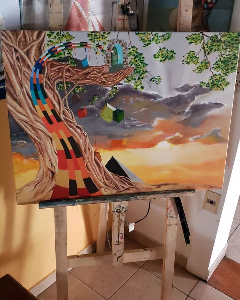 Colorful painting of a tree with a rainbow path, hanging cubes, and a sunset sky, displayed on an easel indoors