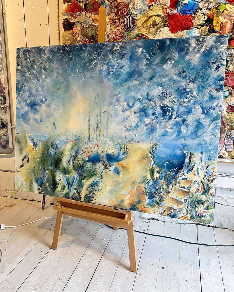 Abstract painting with blue, white, and yellow swirls on a canvas displayed on an easel in an art studio