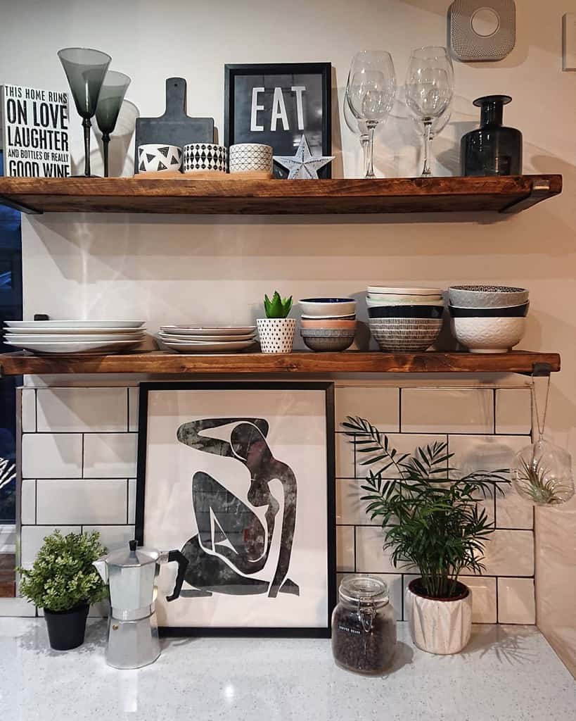 Kitchen shelves with framed art, plates, glasses, plants, and decor items on a tiled backsplash