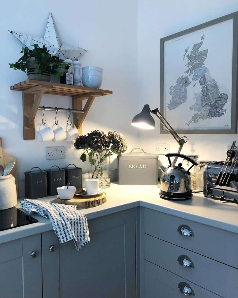 A small wooden shelf with hooks holds mugs, bowls, and decor, adding a cozy touch to this gray and white farmhouse-style kitchen corner