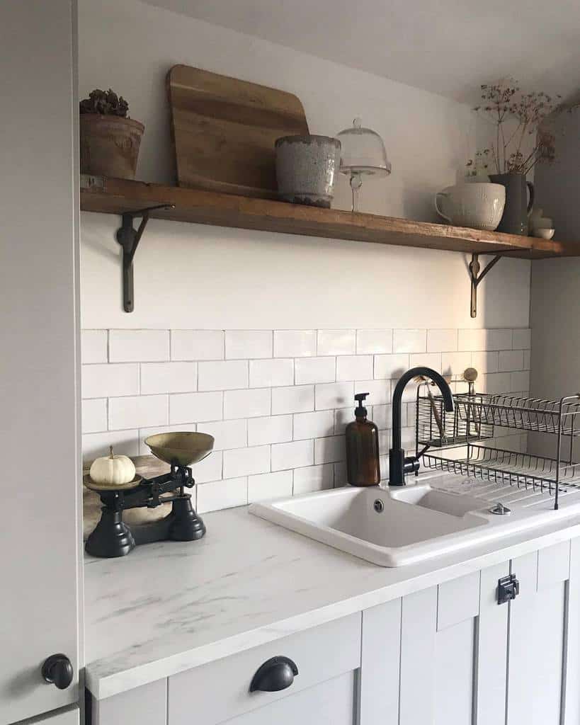 Rustic wooden shelf with black brackets holds cutting boards, ceramics, and decor, adding warmth to a modern farmhouse kitchen with white subway tiles