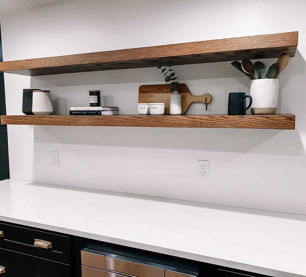 Wooden shelves with decor items and jars above a white countertop, with two electrical outlets visible on the wall