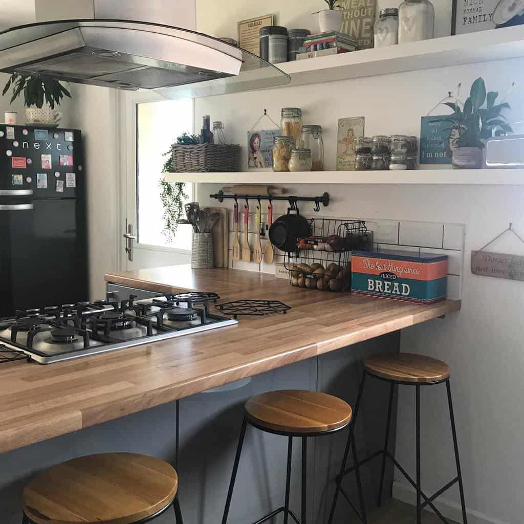 Cozy kitchen with wooden countertops, gas stove, bar stools, shelves with jars and decor, and a black fridge