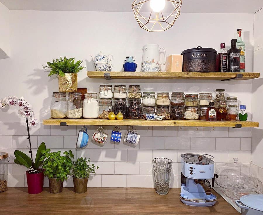 Kitchen shelves with jars of dry goods, plants, hanging mugs, and a coffee maker on the counter below