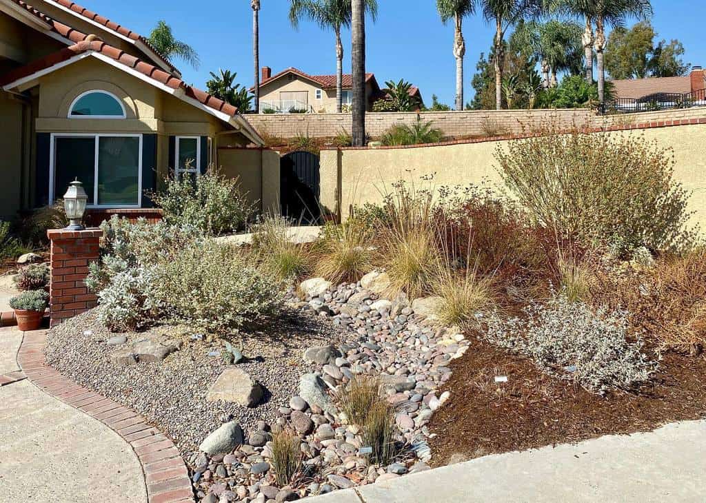 Drought-tolerant front yard xeriscape with native plants, decorative rocks, dry creek bed, and a Mediterranean-style home