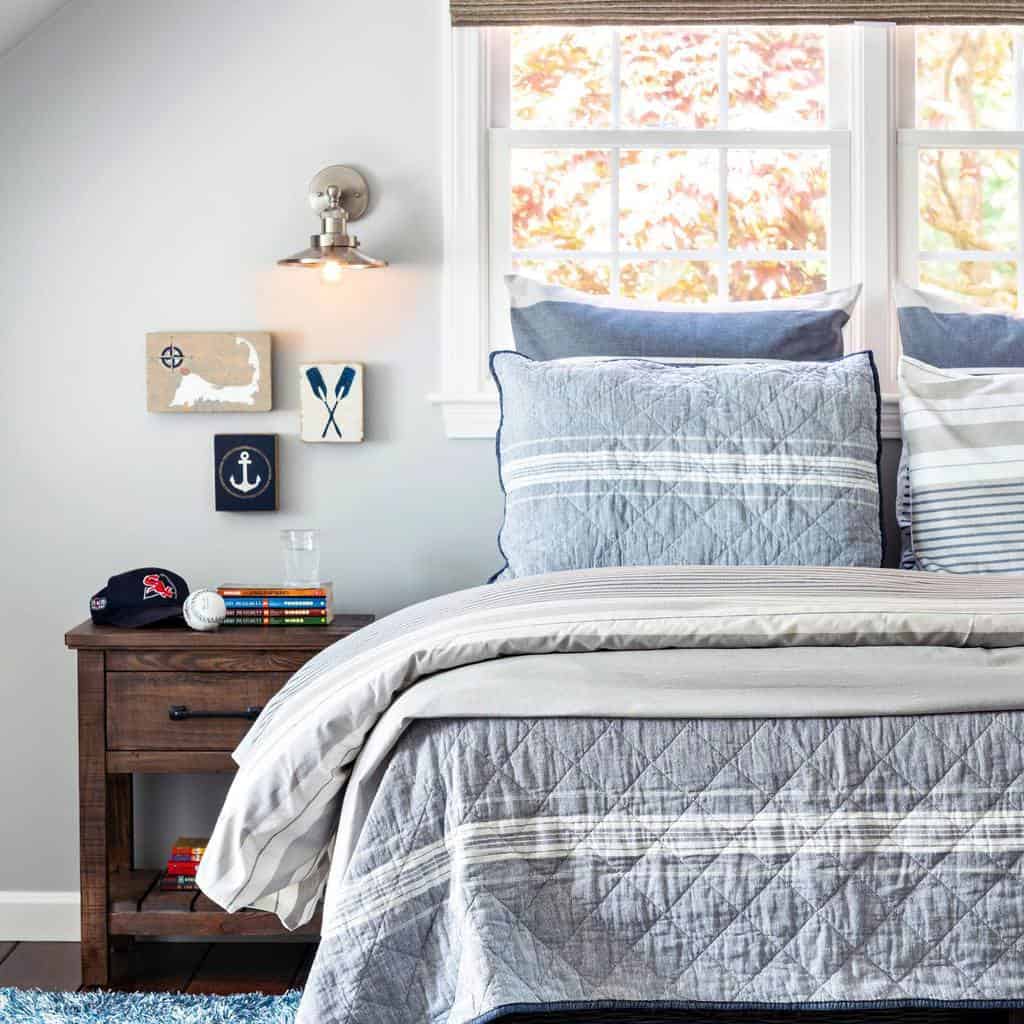 Cozy bedroom with a nautical theme, featuring blue and gray bedding, nautical wall decor, and a wooden nightstand with a lamp