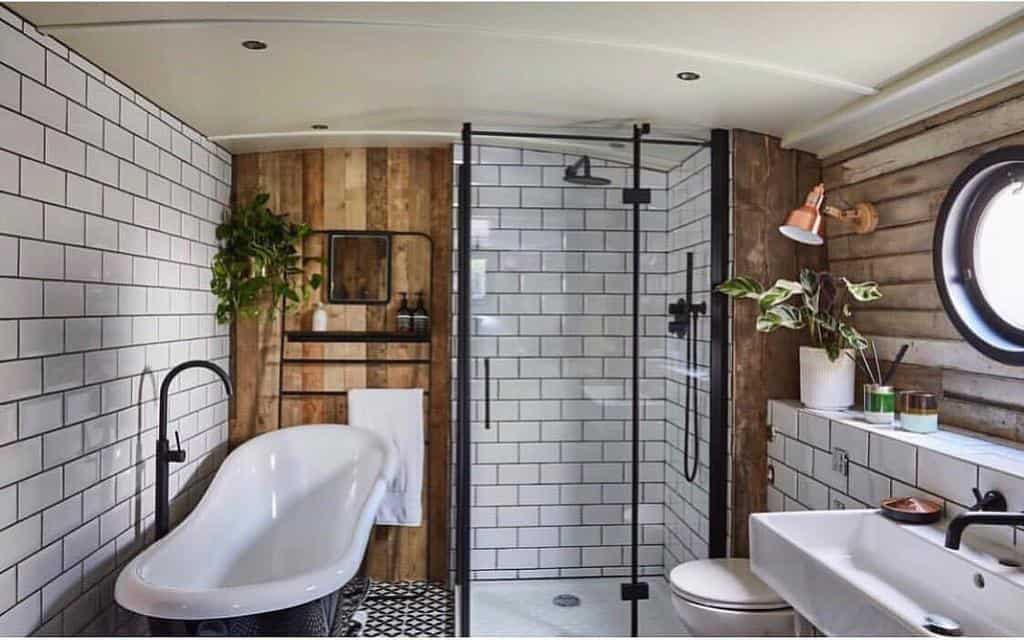 Rustic wet room with subway tiles, wood paneling, a freestanding tub, black fixtures, and porthole window for a cozy, vintage feel