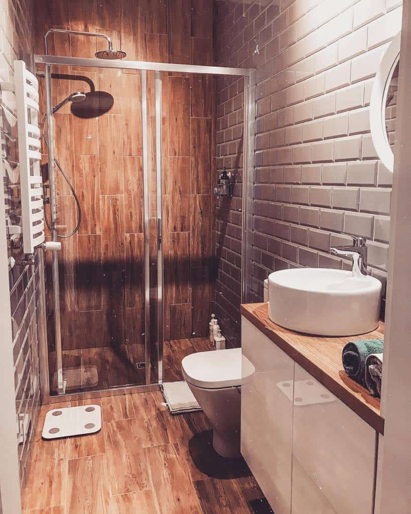 Cozy rustic wet room with wood-look tiles, grey subway walls, a rainfall shower, and a vessel sink on a wood countertop for a warm feel