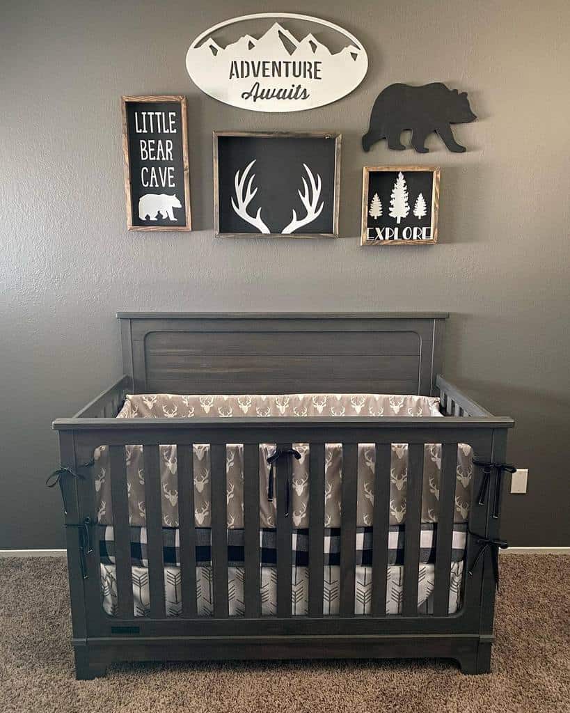 Adventure-themed nursery with a dark wood crib, mountain and wildlife wood signs, and rustic decor featuring bears, antlers, and trees