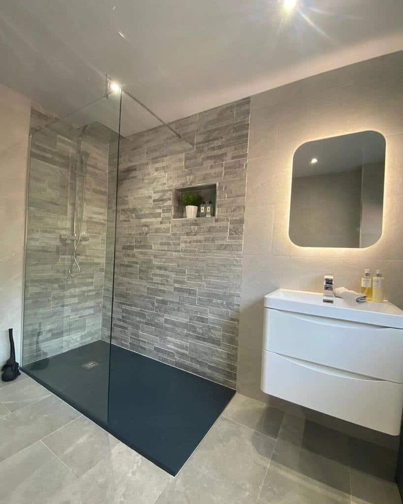 Modern wet room with a sleek glass shower, textured wall tiles, floating vanity with a mirror, and recessed shelf for toiletries