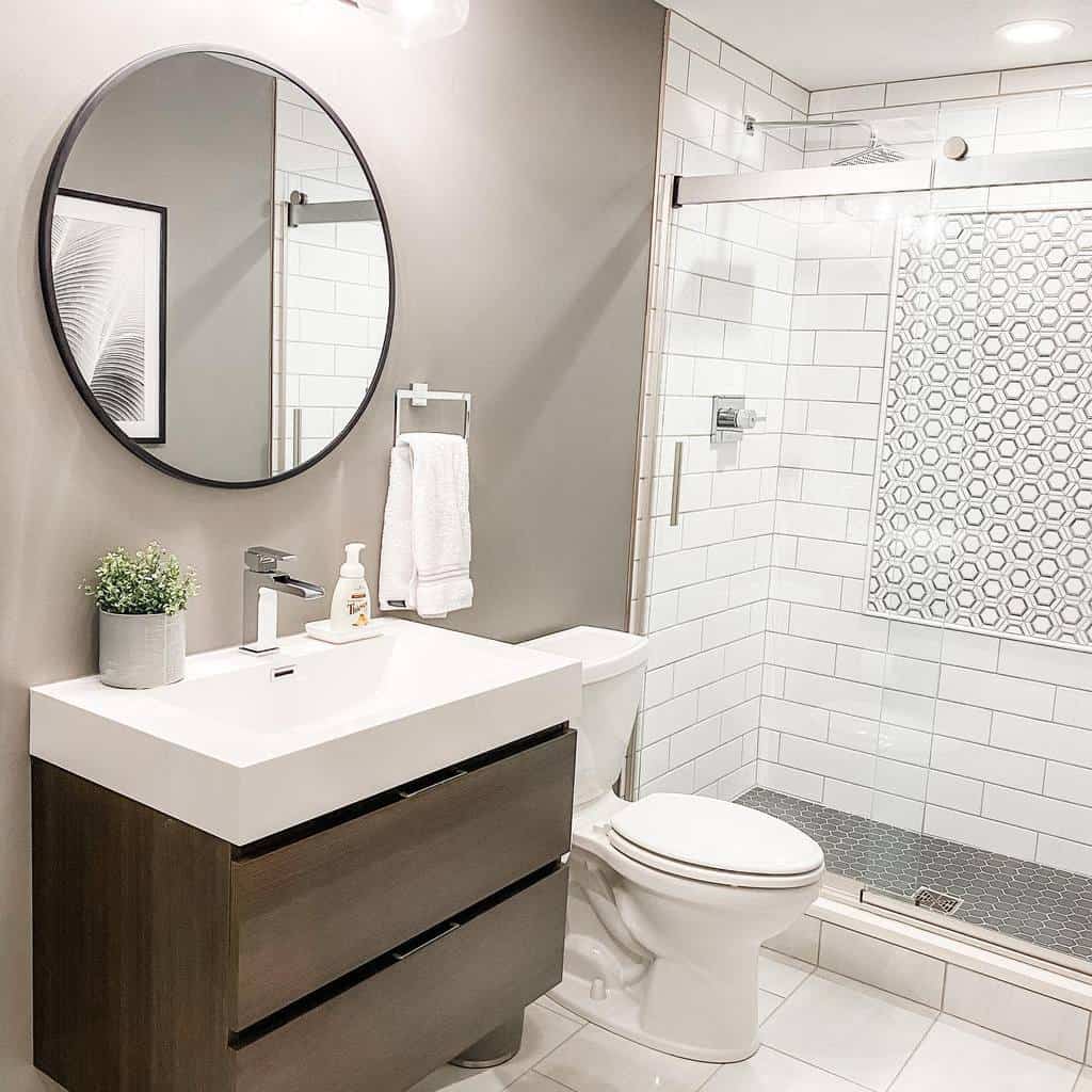 Modern wet room with a floating vanity, round mirror, white subway tiles, and a glass shower enclosure featuring a stylish accent wall