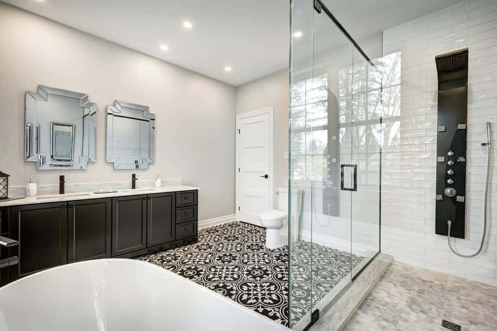 Modern wet room with black and white patterned floor, glass shower, freestanding tub, dual mirrors, and double vanity with dark cabinets