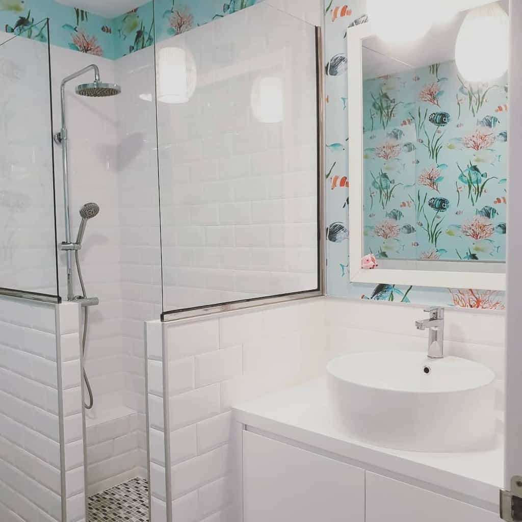 A chic wet room with a glass shower, white subway tiles, and ocean-themed wallpaper featuring a round sink and wall-mounted mirror