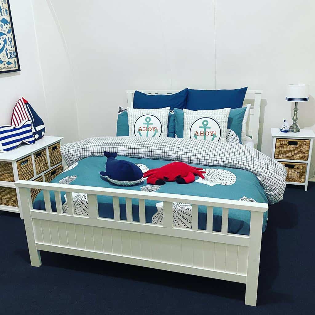 Nautical-themed bedroom with a white bed and anchor pillows, a lamp, and a storage unit; decor includes a plush crab and whale