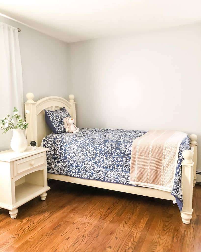 Small coastal bedroom with a white wooden bed, navy patterned bedding, and soft pastel accents, creating a serene and airy beachside feel