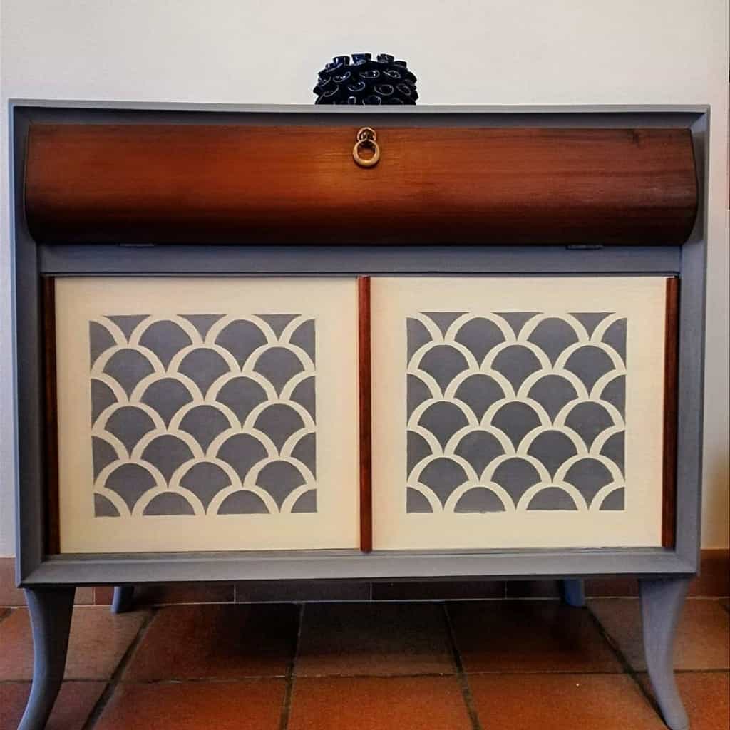 Mid-century modern cabinet with a gray chalk-painted frame, wooden roll-top, and stencil-patterned sliding doors in a scalloped design