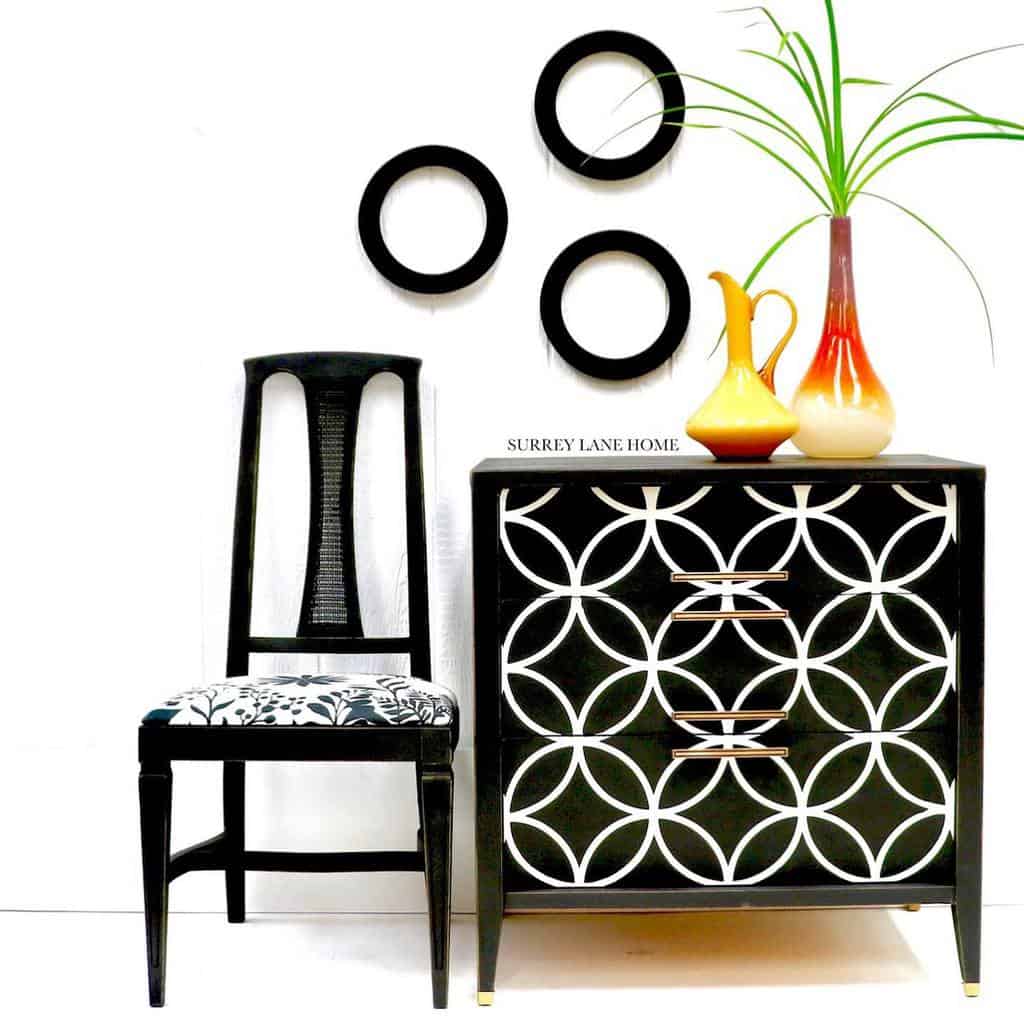 Black and white chalk-painted dresser with a geometric stencil pattern, paired with a vintage chair and decorative accents