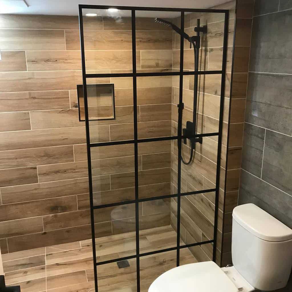 Modern wet room with a black-framed glass shower, wood and gray tiled walls, and a sleek white toilet